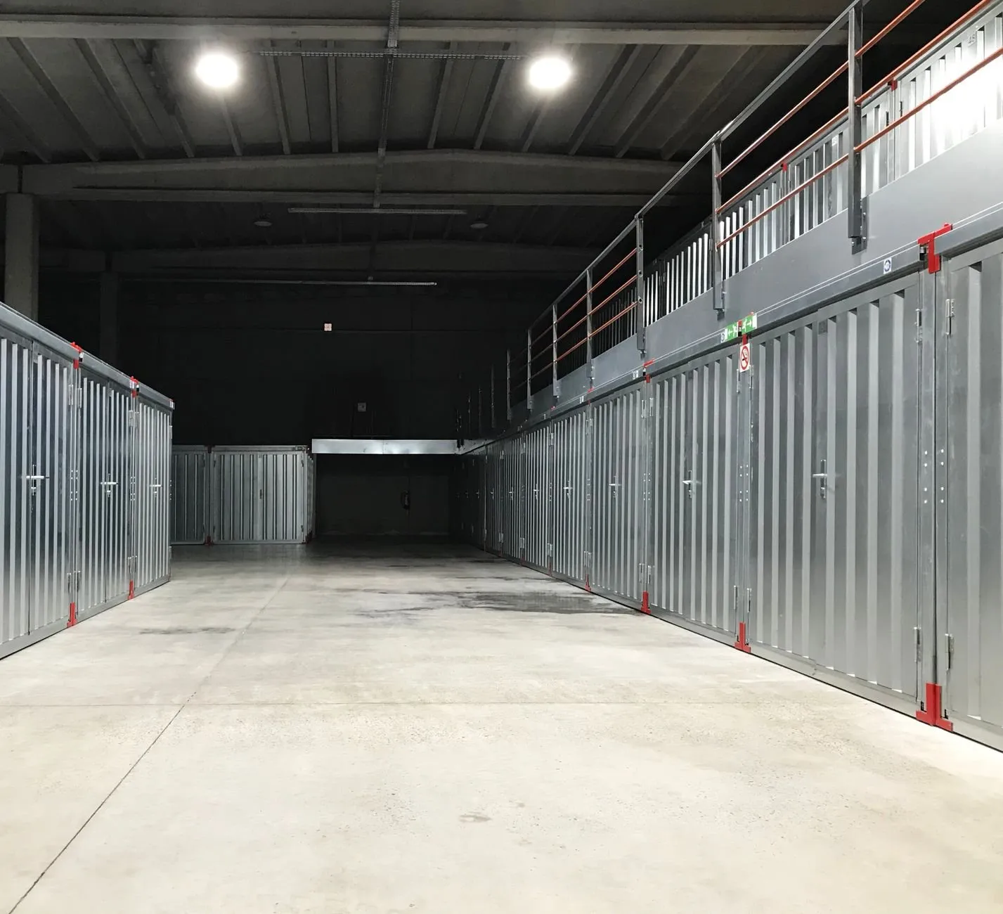 A lit corridor of steel storage units with a walkway above