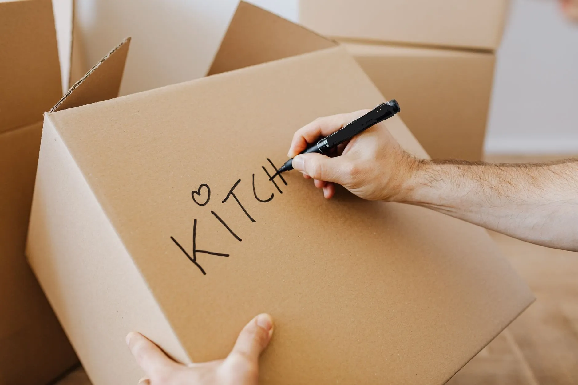 A hand writing KITCHEN on a cardboard box with a black marker