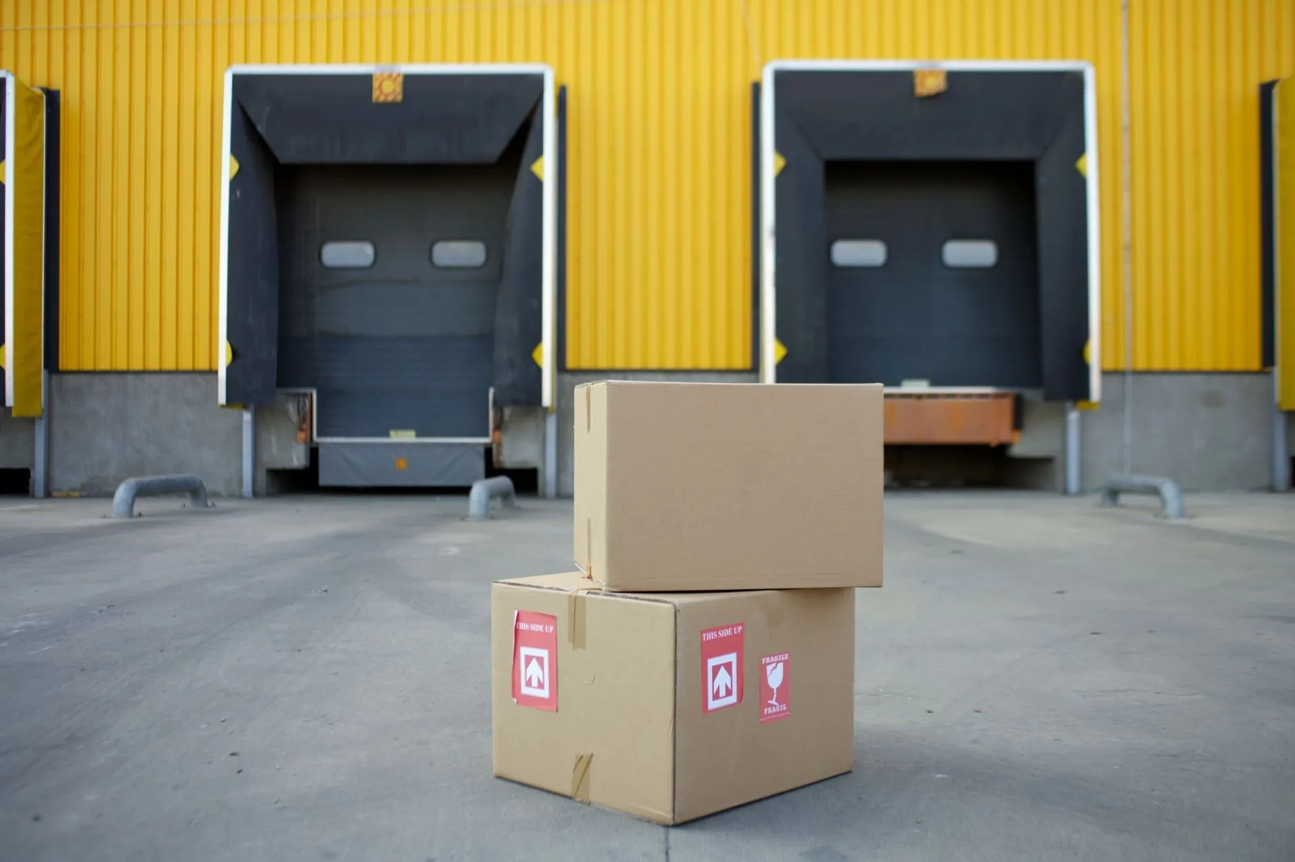Two taped cardboard boxes with this-side-up labels waiting on the apron in front of two loading bay doors