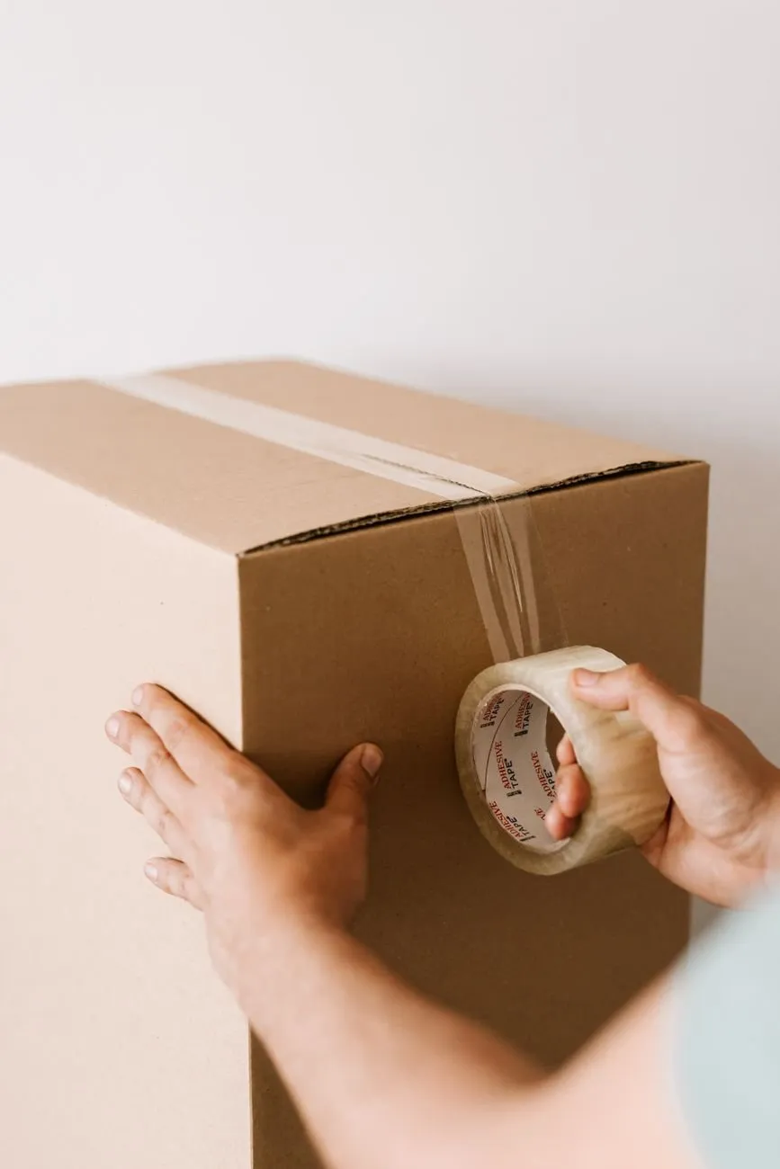 Hands sealing a packed cardboard box with a roll of clear tape